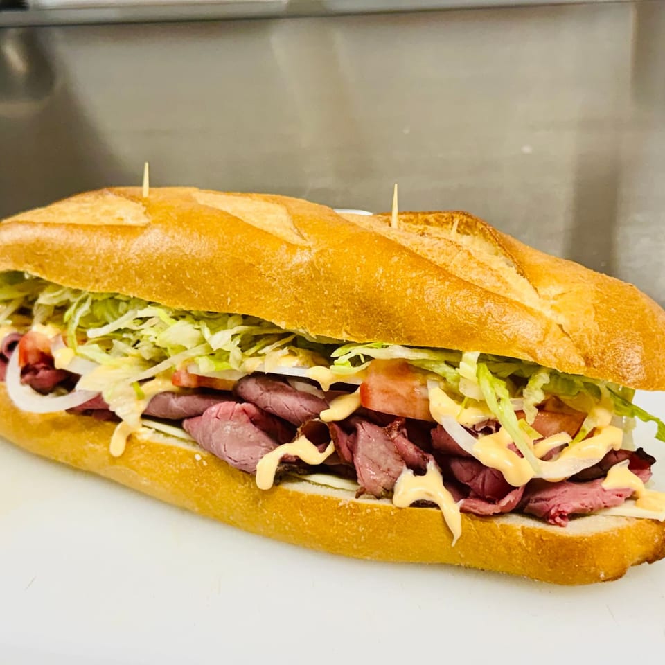 Large roast beef sandwich on a crusty baguette with lettuce, tomatoes, onions, and creamy dressing.